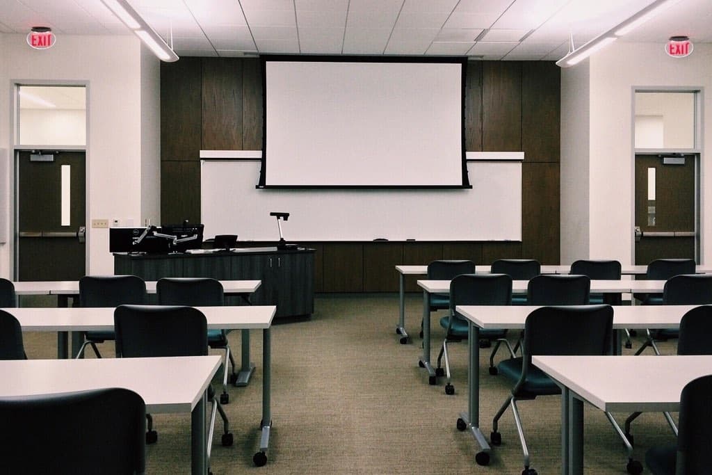 An empty classroom with tables, chairs and a projector screen