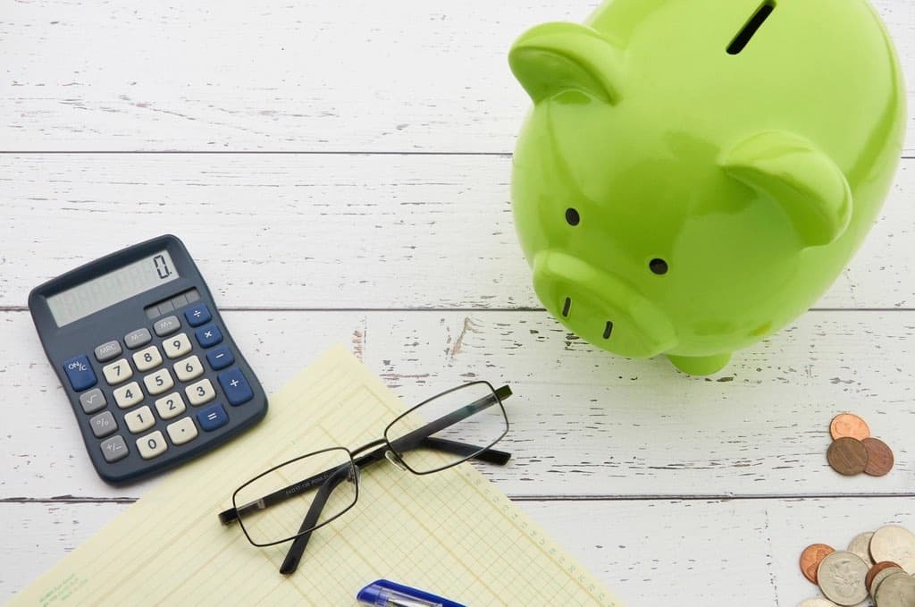 A green piggy bank, a calculator, glasses and coins on a white table