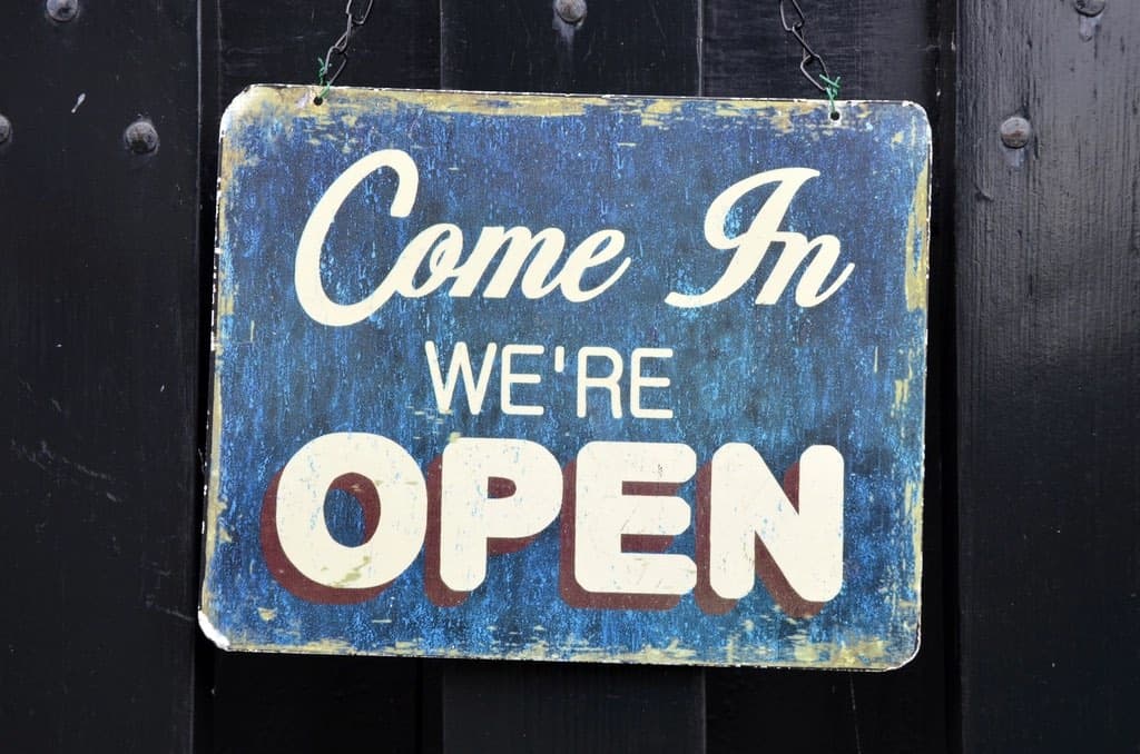 A hand-painted “Come in, we’re open” sign on a dark door